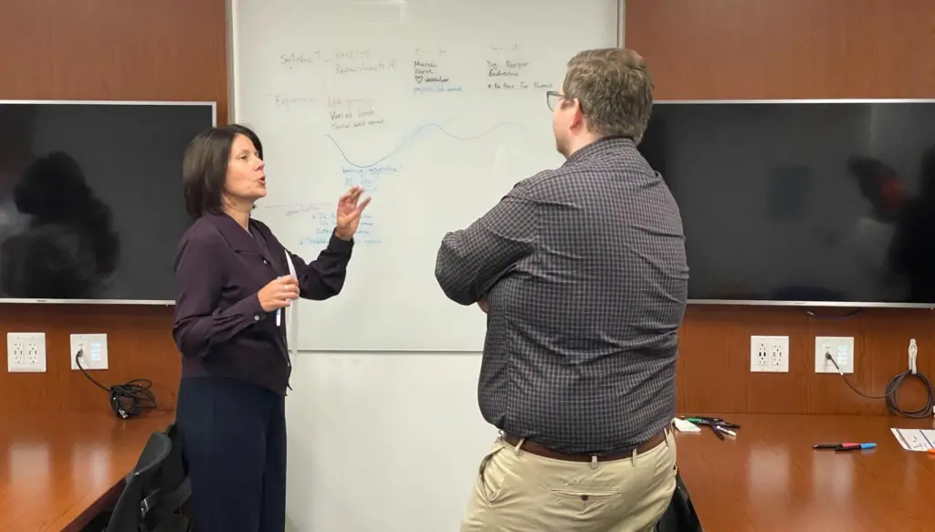 Photo of Lynn DiBenedetto and Kyle Johnson talking in front of whiteboard